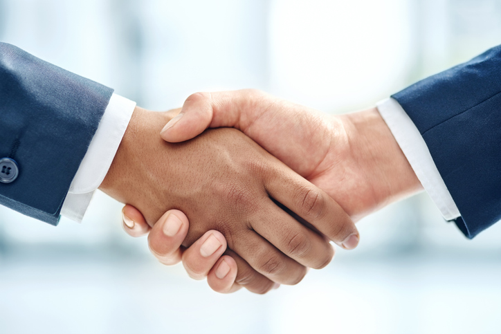 Two people shaking hands over a business meeting table